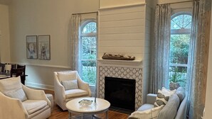 A spacious living room with a fireplace, two white armchairs, a sofa, and a ceiling fan. - Spacious family friendly 4-bedroom house in beautiful Porters Neck, Wilmington (Wilmington)