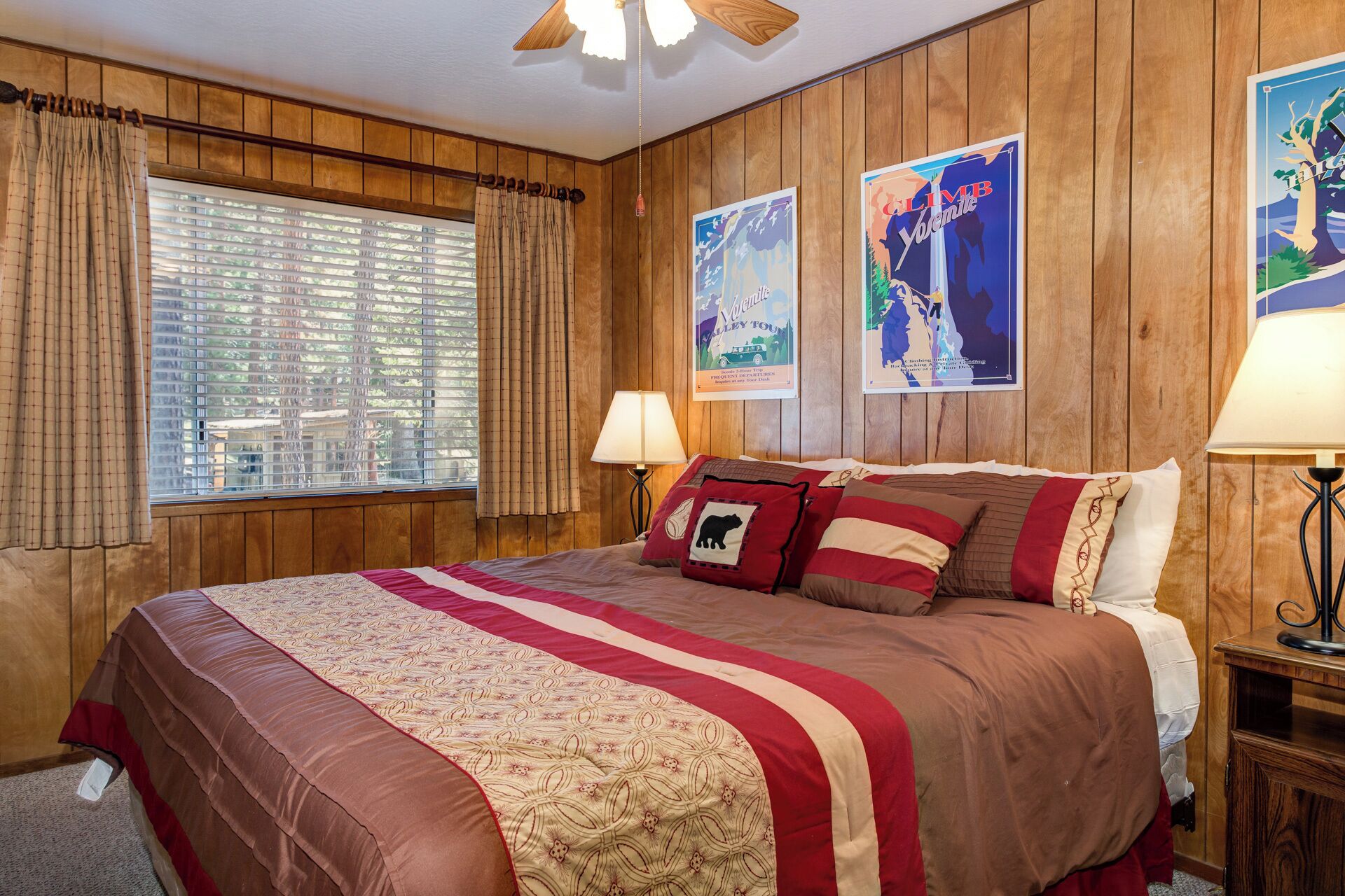 Camera d'albergo con un letto grande, pareti in legno, due poster e una finestra con tende.