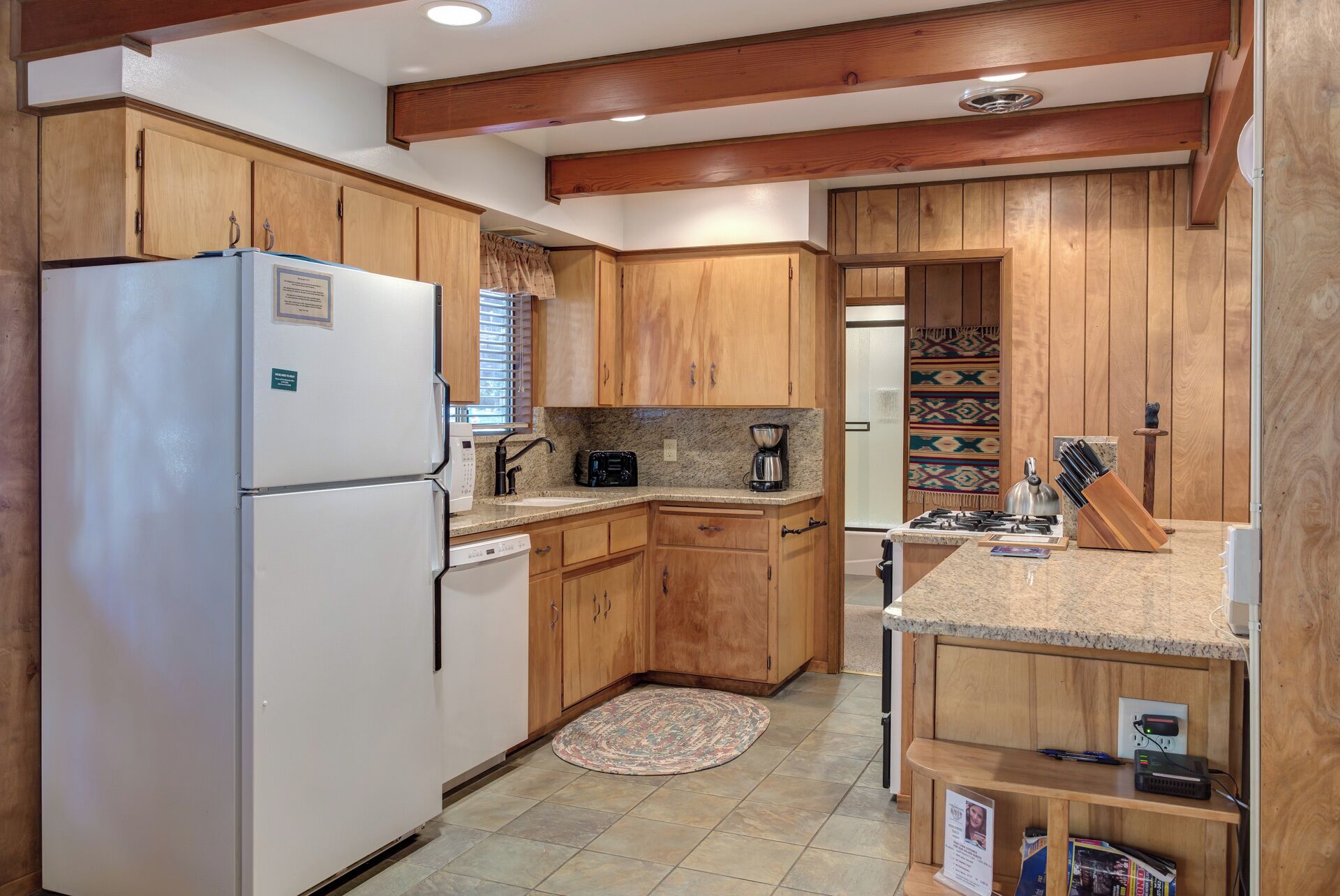 Cocina compacta con armarios de madera, un refrigerador blanco, una cafetera y una estufa a gas.