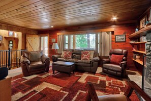 A cozy cabin interior with a wooden ceiling, leather furniture, and a large window with curtains. - Bradley's Cabin (Yosemite National Park)