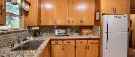 A kitchen with wooden cabinets, a granite countertop, a sink, a toaster, and a refrigerator.