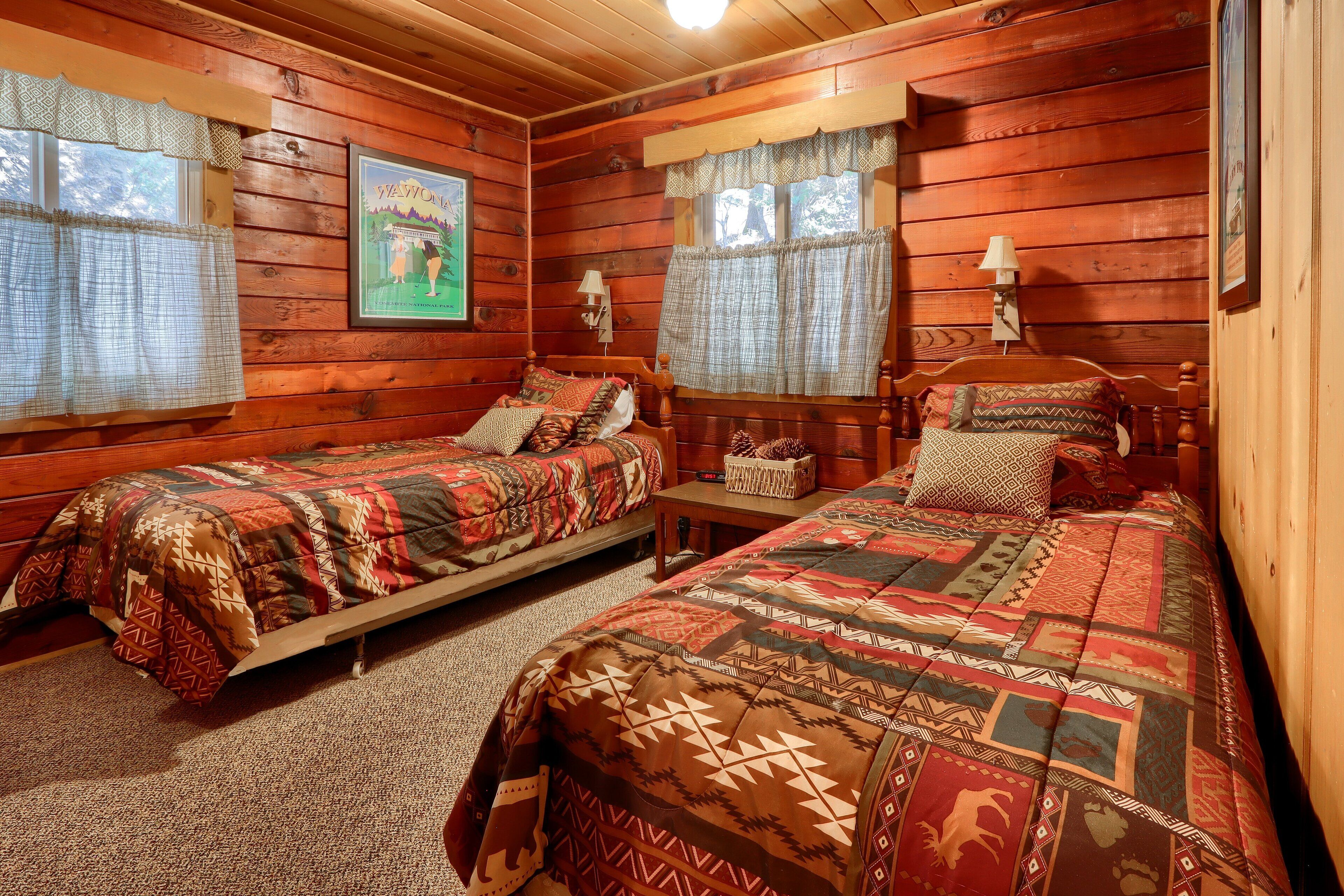 A cabin-style room with two beds, wooden walls, and a framed picture on the wall.