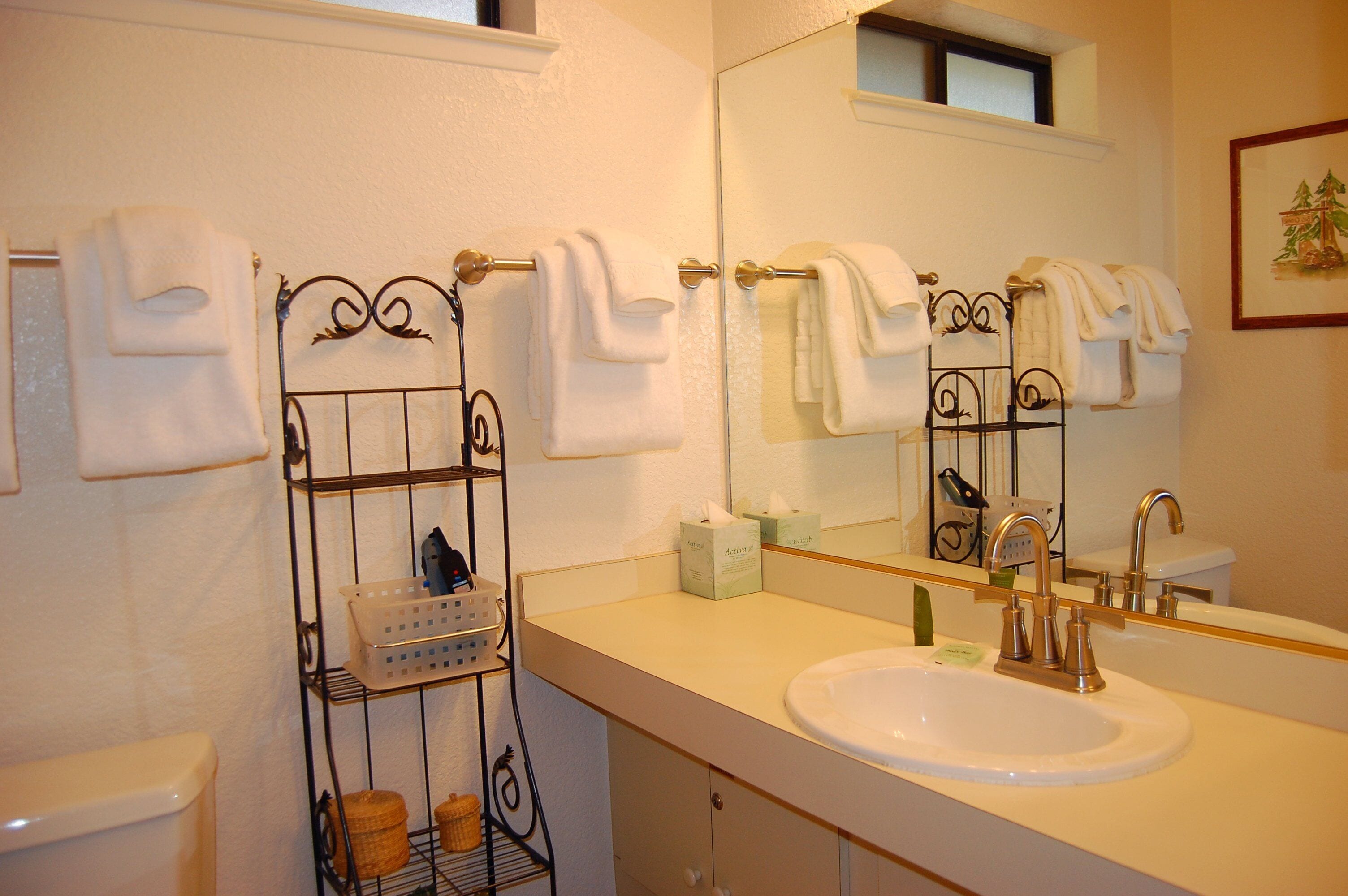 A bathroom with a white sink, a mirror, and a towel rack with multiple towels.