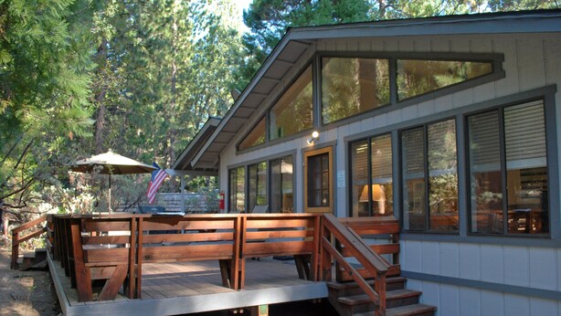 Une maison moderne dotée d’une terrasse en bois, de grandes fenêtres et d’un escalier menant à l’entrée.