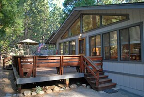 A modern house with a wooden deck, large windows, and a staircase leading to the entrance. - Big Cedar (Yosemite National Park)