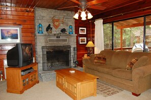 A living room with a fireplace, wooden walls, a television on a stand, and a couch. - Cubby's Den (Yosemite National Park)