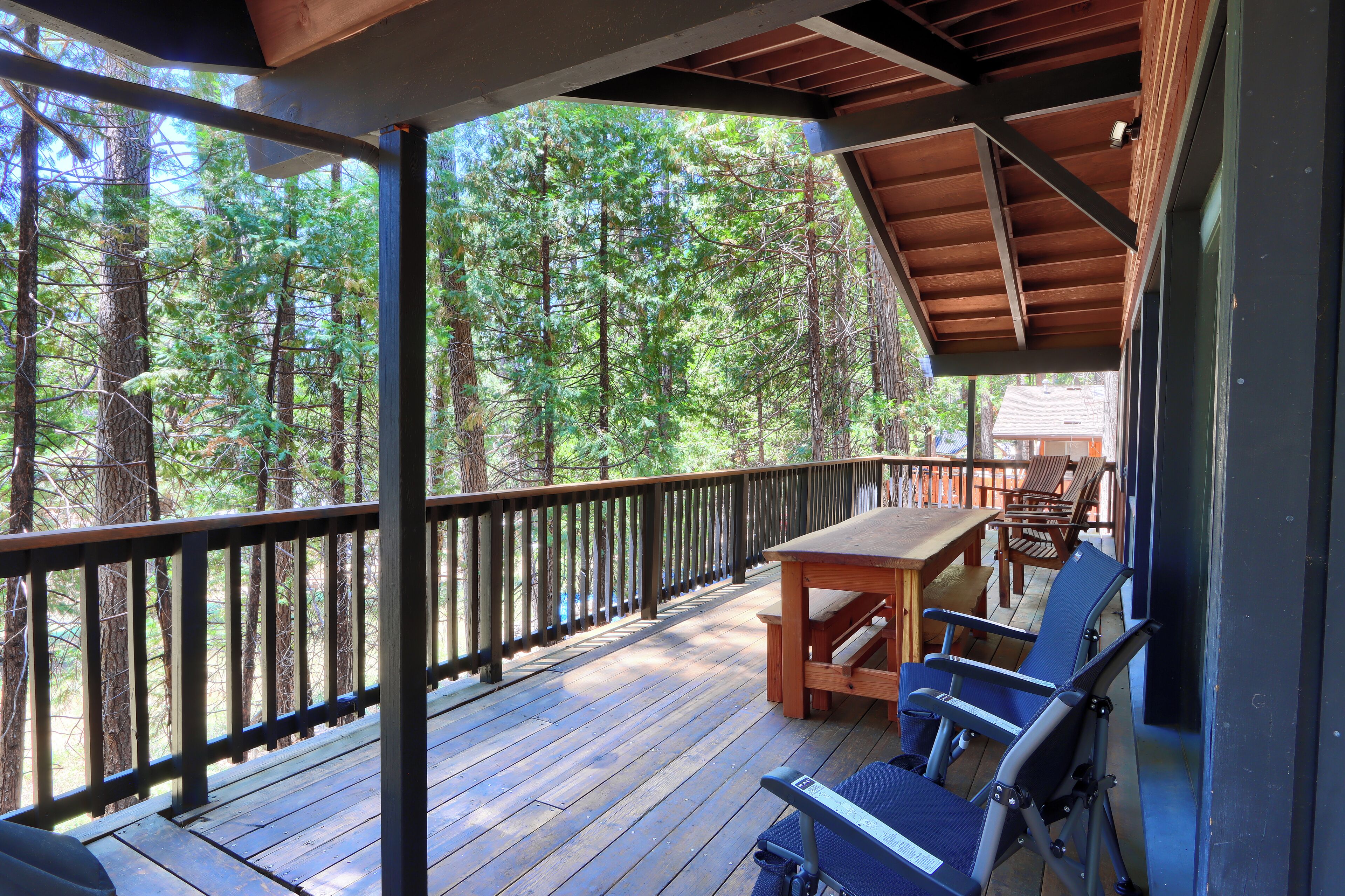 A wooden deck with a table and chairs, overlooking a forest.