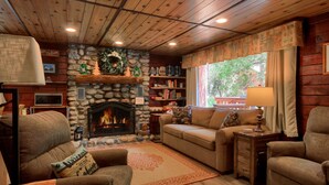 A cozy living room with a stone fireplace, wooden ceiling, and a large window with curtains. - Chipmunks Holiday (Yosemite National Park)