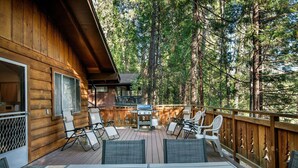 Un patio in legno con mobili da esterno, un barbecue e vista su una zona boschiva.