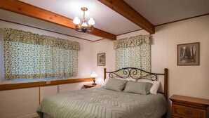Una camera da letto con un letto, un comodino, una cassettiera, una finestra con tende floreali e un lampadario.