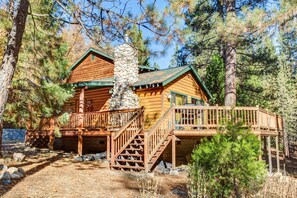 A log cabin with a stone chimney, wooden deck, and a staircase leading to the entrance. - River Refuge (Yosemite National Park)