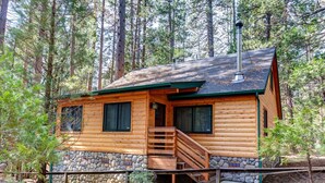 Une cabane en rondins avec des fondations en pierre, une terrasse en bois et un escalier menant à l’entrée.