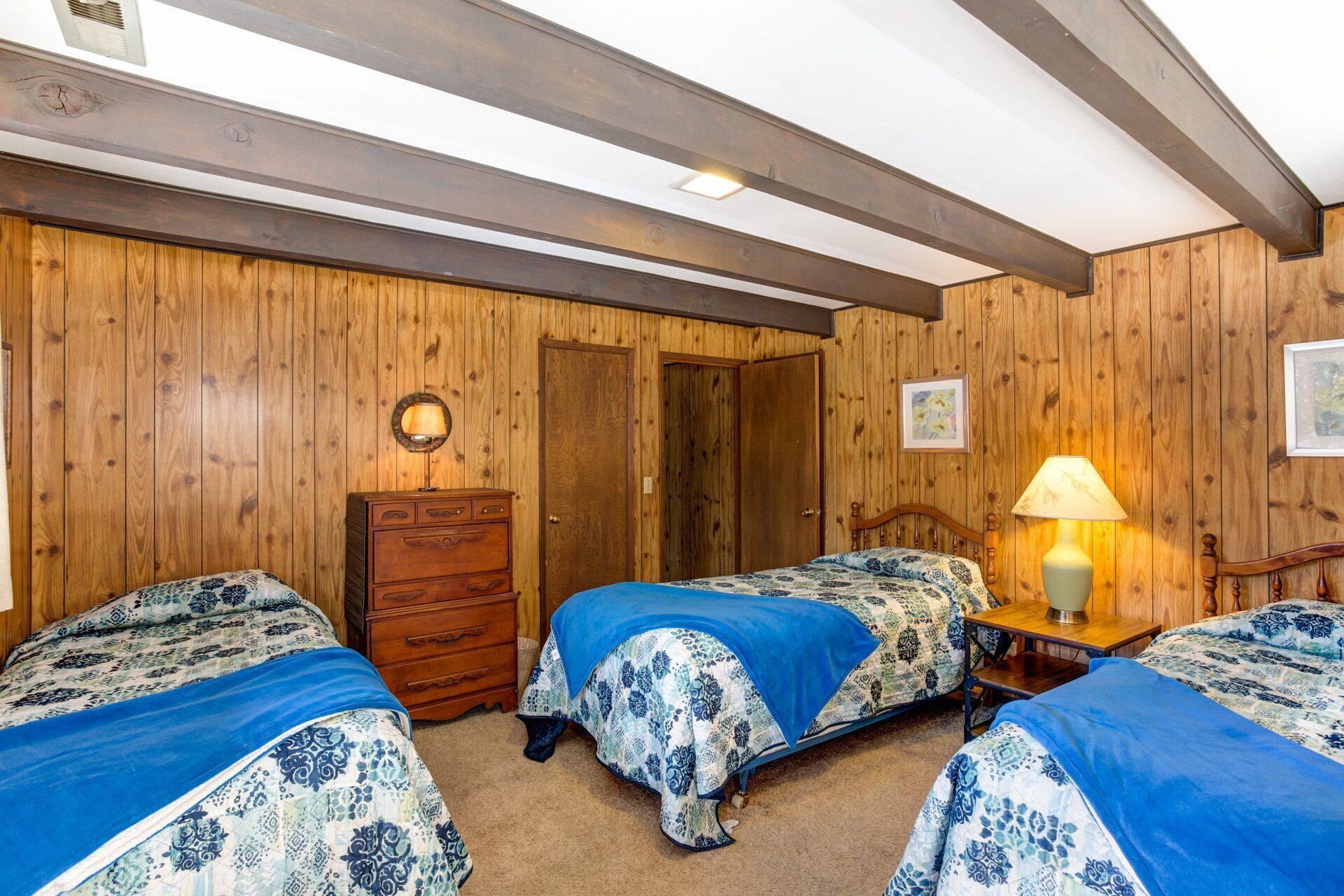 Een kamer met houten wanden, twee bedden met blauw-witte beddengoed, een houten dressoir en een nachtkastje met een lamp.
