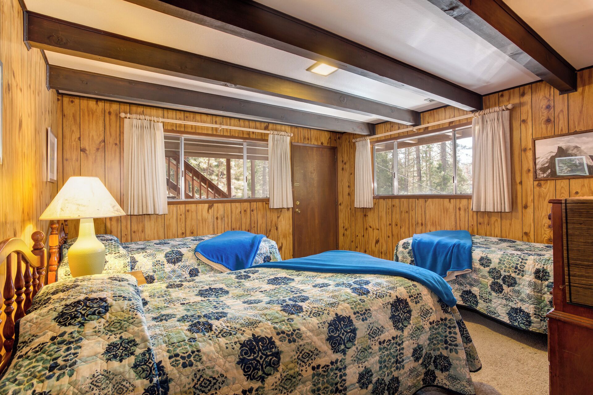 A cabin-style bedroom with two beds, wooden walls, and large windows.