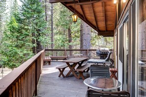 Eine Holzdielen-Terrasse mit Picknicktischen und Grill, umgeben von Bäumen.