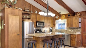A kitchen with wooden cabinets, a stainless steel refrigerator, a microwave, and a large island with stools. - Star Gazers (Yosemite National Park)