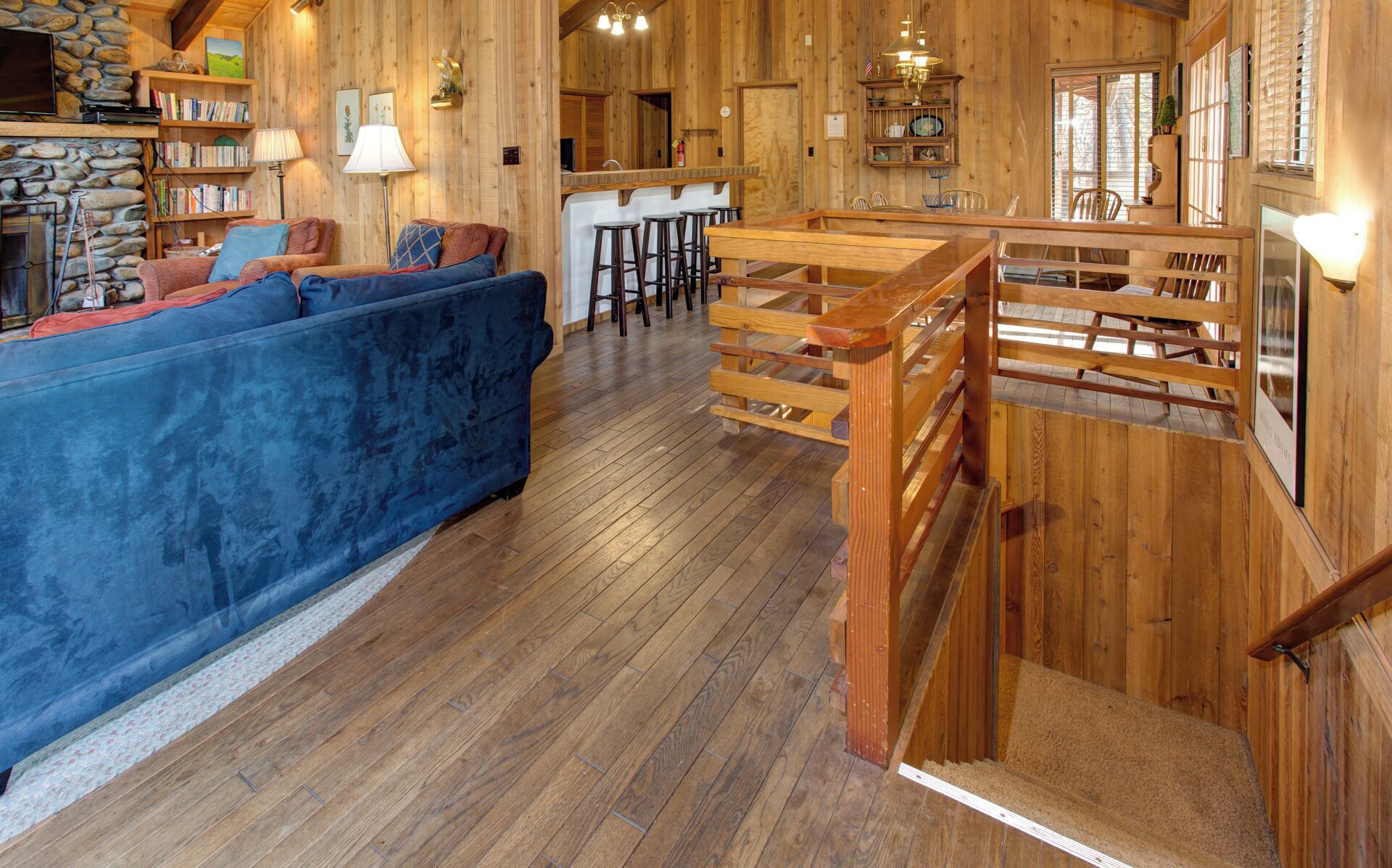 A rustic interior with a blue sofa, wooden bar, and stone fireplace.