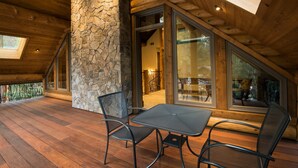 A wooden deck with a stone pillar, a table with chairs, and large windows. - Rustic Retreat (Yosemite National Park)