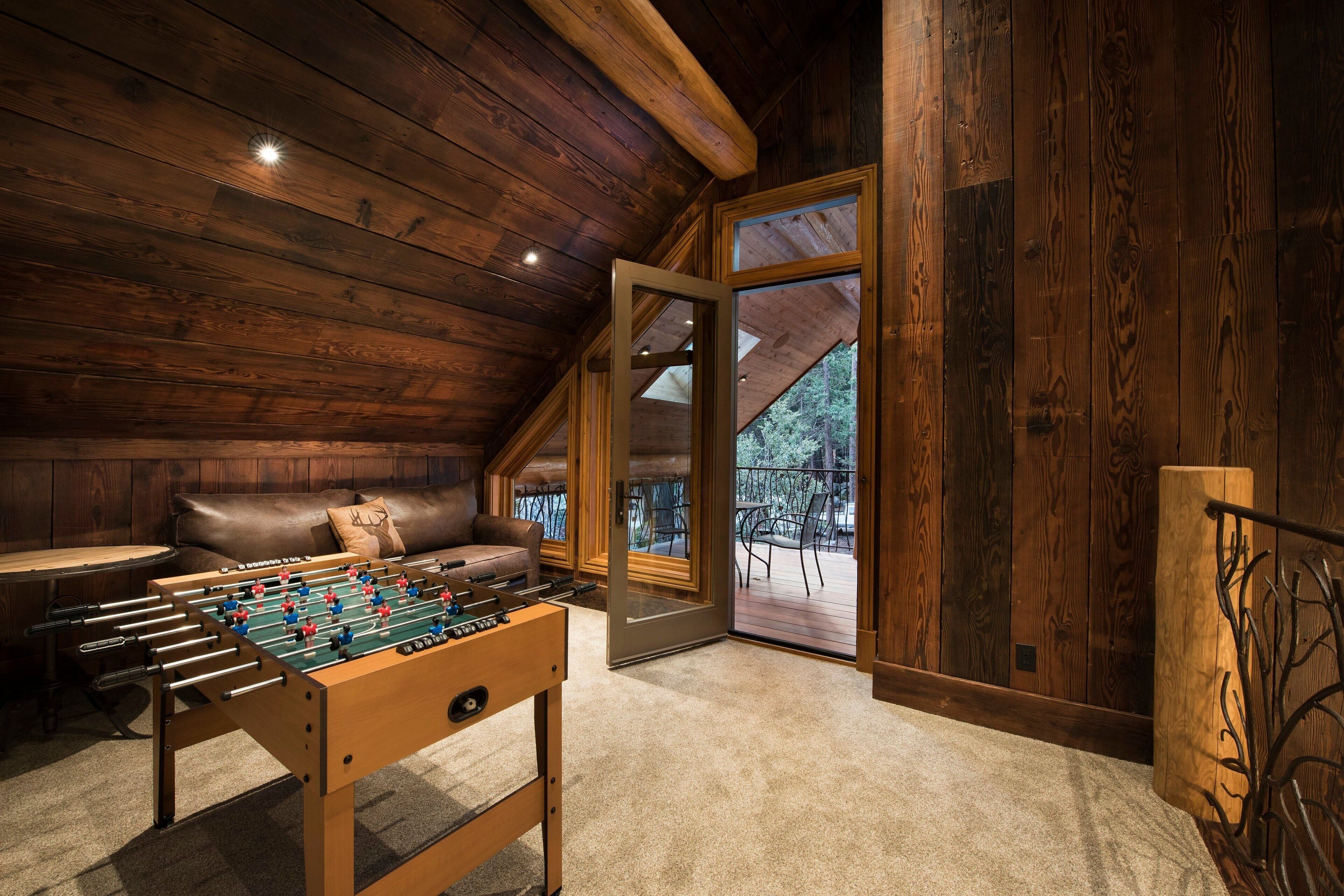 A cozy room with a foosball table, a leather sofa, and a large window offering a view of the outdoors.