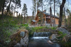 A log cabin with a waterfall in front, surrounded by tall trees. - Rustic Retreat (Yosemite National Park)