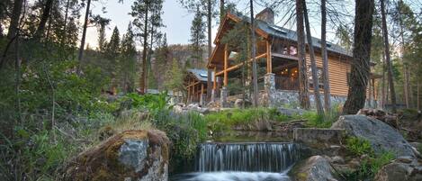 Une cabane en rondins avec une cascade en contrebas, entourée de grands arbres.