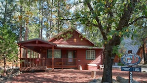 A red cabin with a porch, surrounded by trees and a sign indicating it's The Redwoods in Yosemite. - Black Oak Lodge (Yosemite National Park)