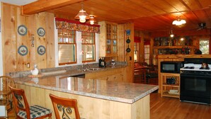 A wooden cabin interior with a kitchen, dining area, and a large island with bar stools. - Black Oak Lodge (Yosemite National Park)