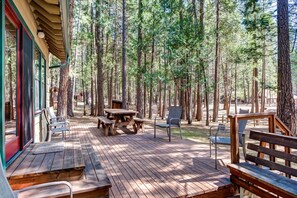 A wooden deck with picnic tables and chairs, surrounded by tall pine trees. - Wawona Retreat (Yosemite National Park)