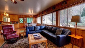 A cozy living room with a leather sofa, a red armchair, a coffee table, and a dining area with a table and chairs. - Longview (Yosemite National Park)