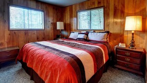 A wooden-paneled bedroom with a large bed, two bedside lamps, and a nightstand with a phone. - Longview (Yosemite National Park)