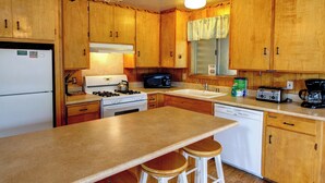 A kitchen with wooden cabinets, a stove, microwave, sink, and a dishwasher. There are stools at the counter. - Longview (Yosemite National Park)