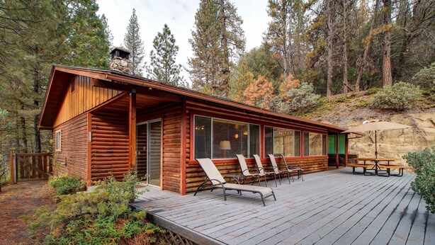 A log cabin with a deck, outdoor seating, and a stone chimney. - Longview (Yosemite National Park)