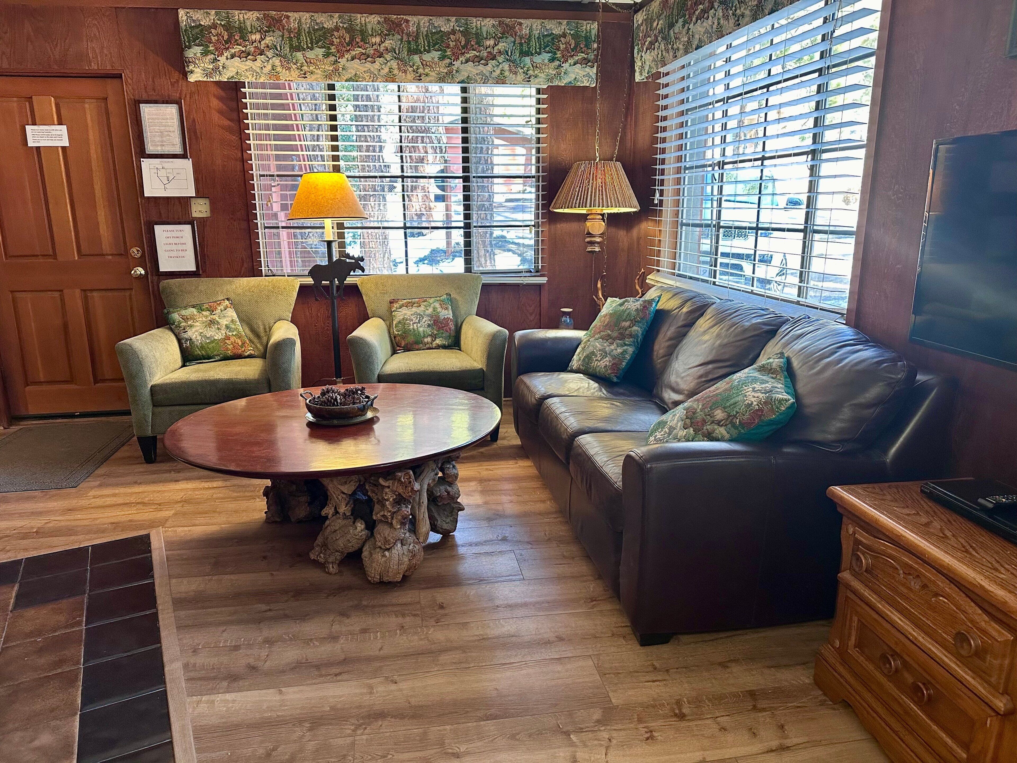 Un salon chaleureux avec un canapé en cuir marron, deux fauteuils, une table basse en bois et un téléviseur.