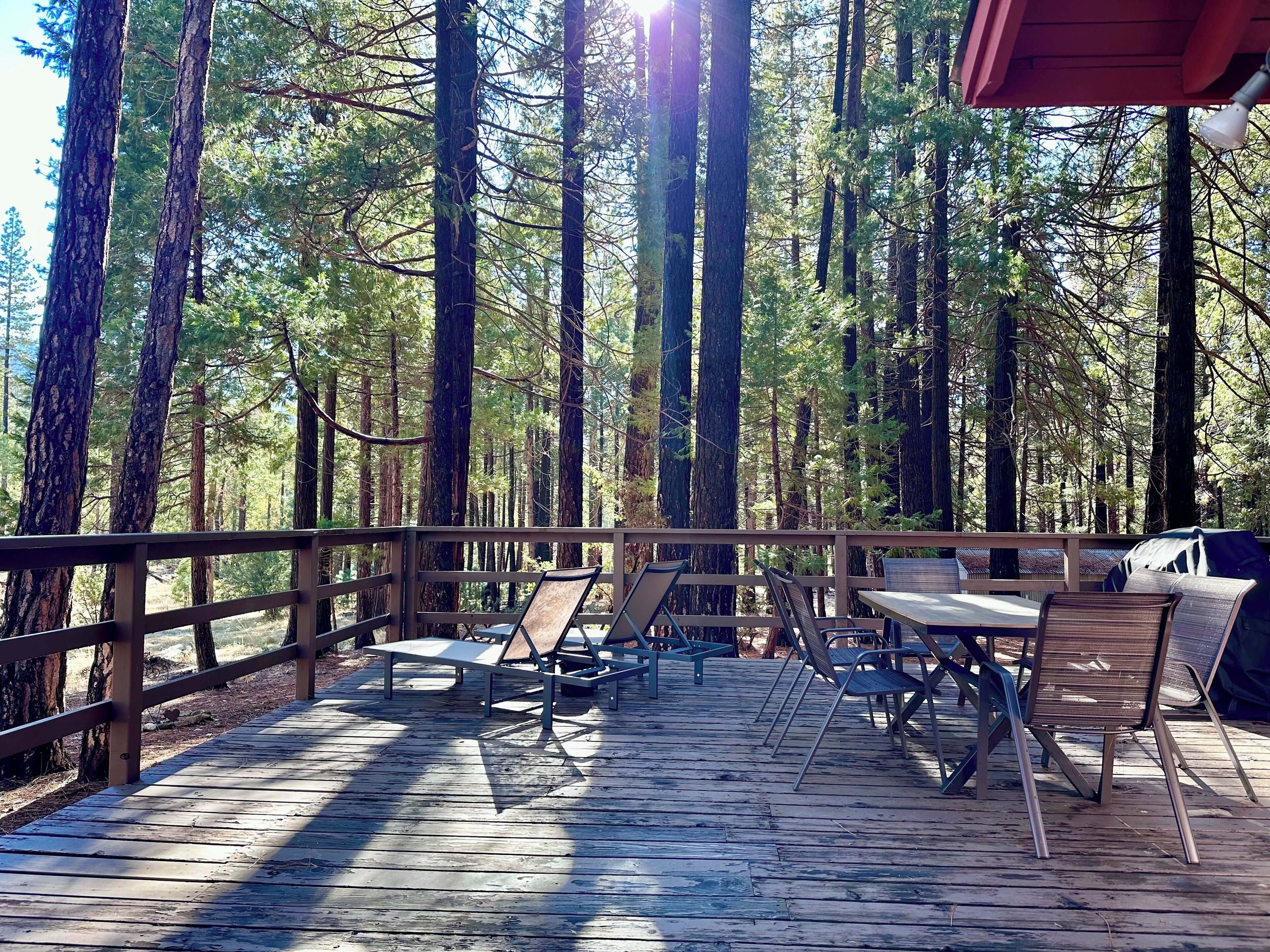 A wooden deck with metal chairs and tables, surrounded by tall trees.