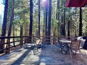 A wooden deck with metal chairs and tables, surrounded by tall trees. - Heart of the Meadow (Yosemite National Park)