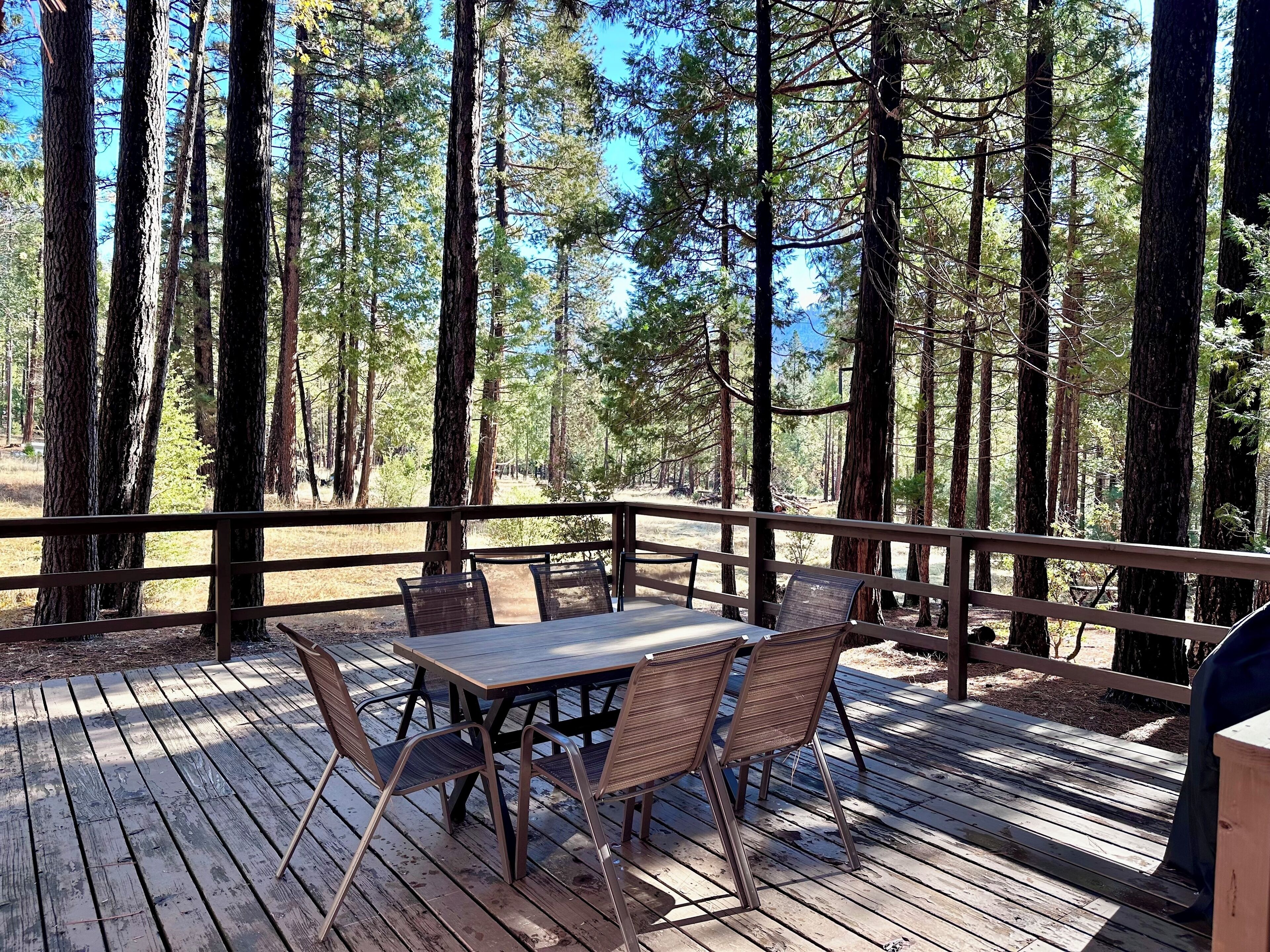 A wooden deck with a table and chairs, surrounded by tall trees.