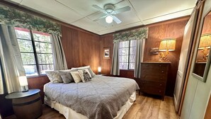 A bedroom with a bed, wooden flooring, a ceiling fan, a nightstand, a dresser, and windows with curtains. - Heart of the Meadow (Yosemite National Park)