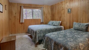 A room with wooden walls, two beds with patterned bedding, a window with curtains, and a small desk. - Villarreal Retreat (Yosemite National Park)