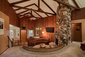 A cozy living room with a stone wall, wooden ceiling beams, a fireplace, and a television mounted on the wall. - Villarreal Retreat (Yosemite National Park)