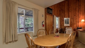 A dining area with a wooden table and chairs, a fire extinguisher on the wall, and a wooden paneled wall with a framed picture. - Villarreal Retreat (Yosemite National Park)
