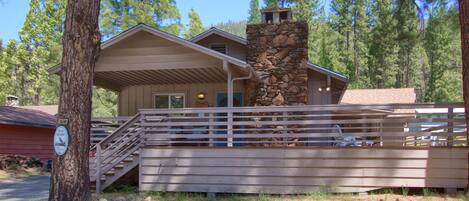 A lodge with a stone chimney, wooden deck, and a staircase leading to the entrance.