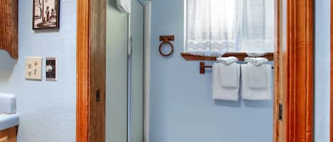 A bathroom with a shower, a toilet, a sink, and a window with a curtain.