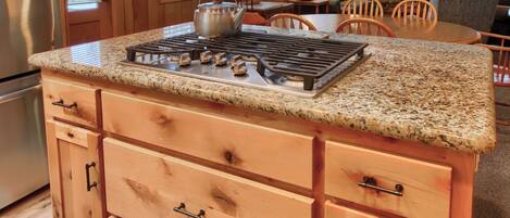 A kitchen with a granite countertop, wooden cabinets, a stainless steel refrigerator, and a stone fireplace.