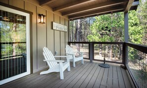 A covered porch with two Adirondack chairs, a welcome sign, and a view of a forested area. - Hilltop Haven (Yosemite National Park)