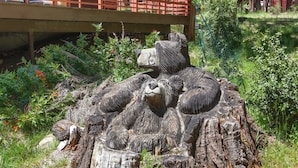 En stor träskulptur som föreställer björnar, placerad på en trädstam i en trädgårdsmiljö.