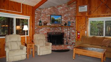 A cozy living room with a fireplace, wooden furniture, and a television mounted above it.
