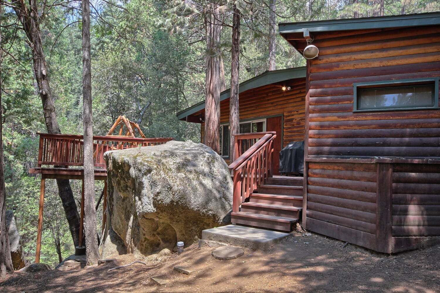 Une cabane en rondins avec une terrasse en bois et un escalier menant à l’entrée.