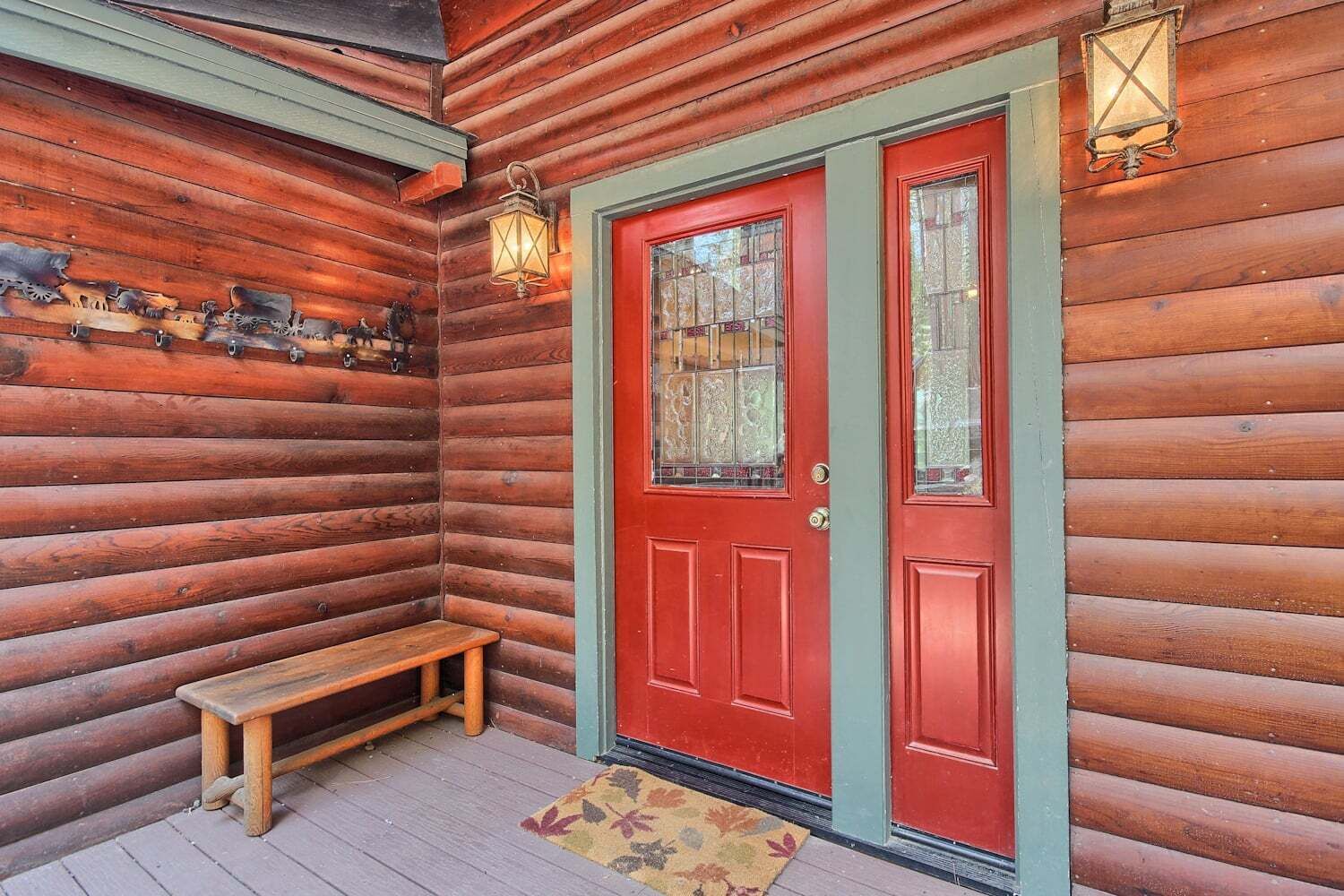 Una cabaña de madera con puerta roja, un banco y dos faroles fijados a la pared.