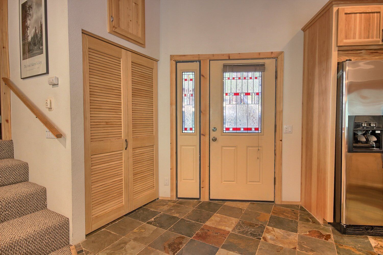 A kitchen with a refrigerator, wooden cabinets, a double door with a glass window, and a staircase leading to a landing.