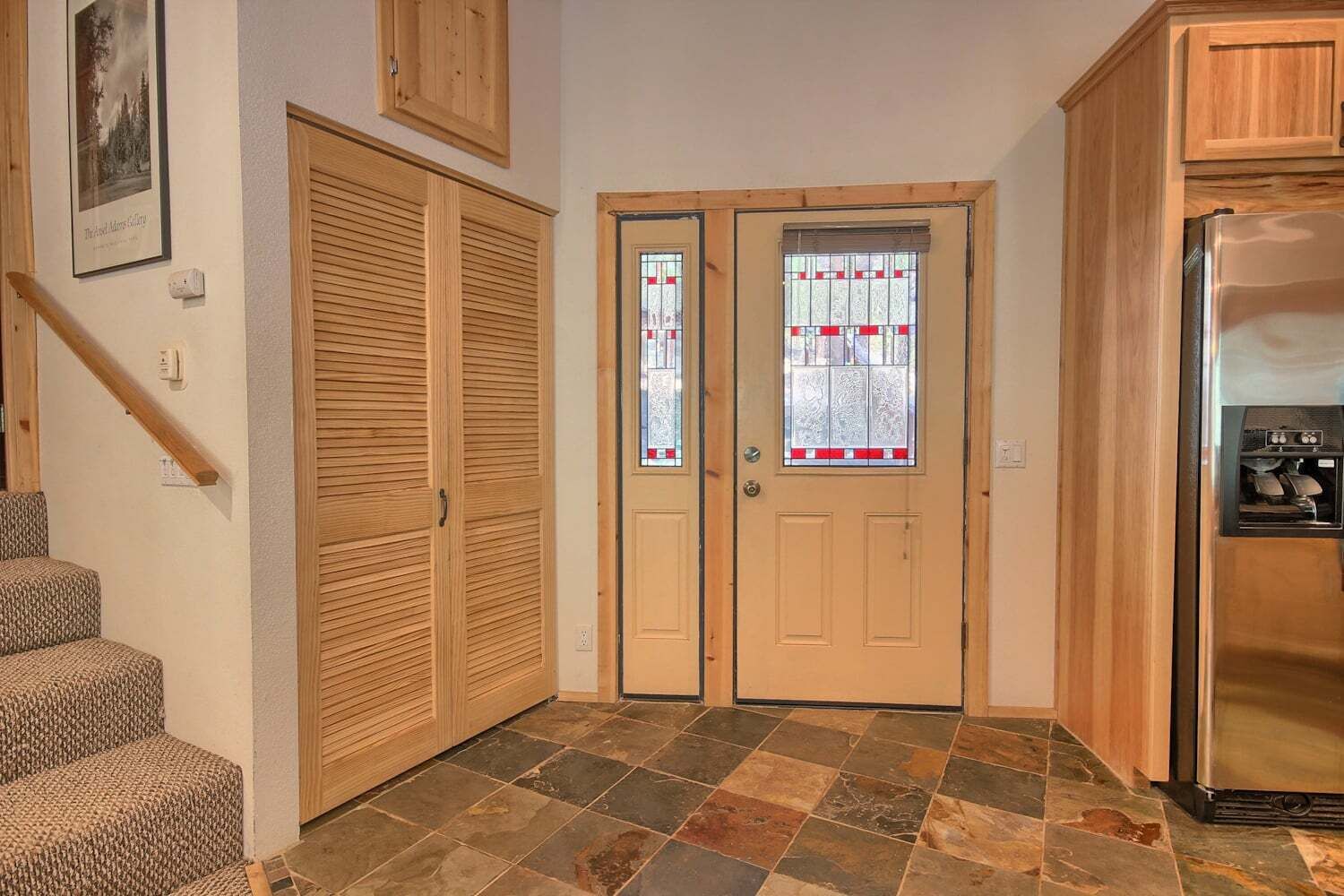 A kitchen with a refrigerator, wooden cabinets, a double door with stained glass, and a staircase.